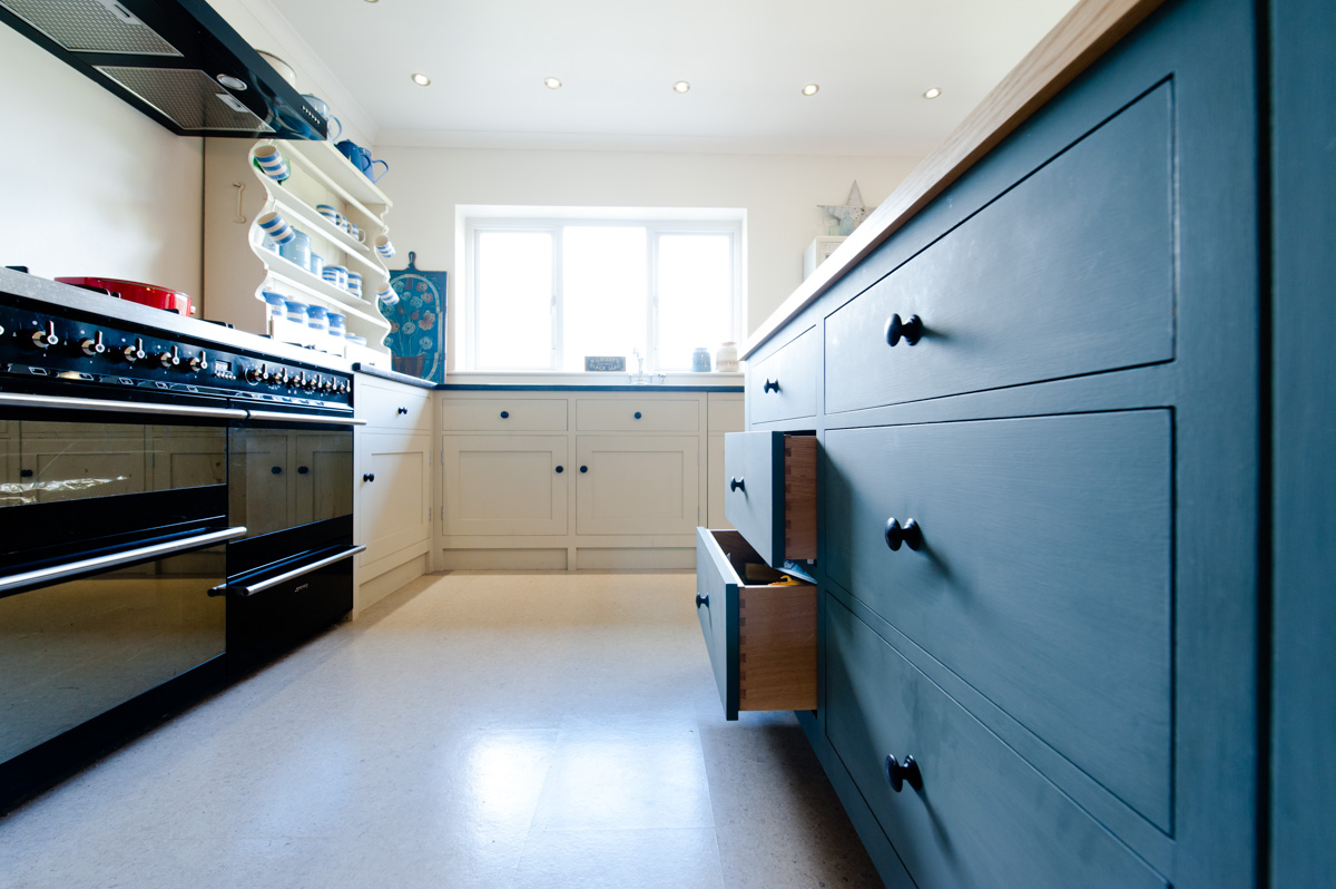 A white painted bespoke timber kitchen with a grey timber island finished with a white worktop